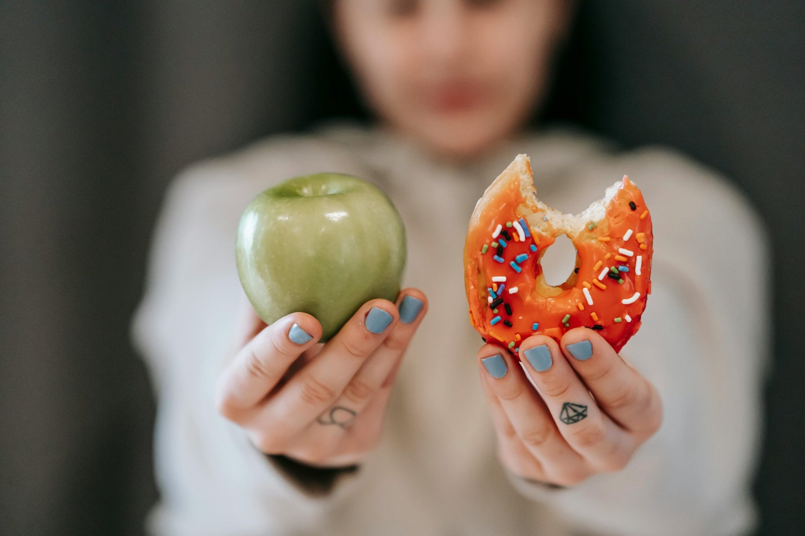 Person holding a green apple in one hand and a partially eaten donut in the other, symbolizing the choice between healthy and unhealthy foods in a low-sugar diet plan.