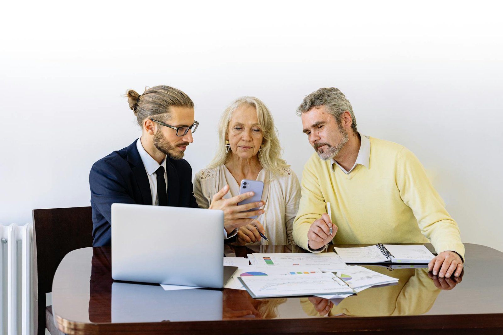 Three people reviewing insurance documents and details on a smartphone while seated at a table