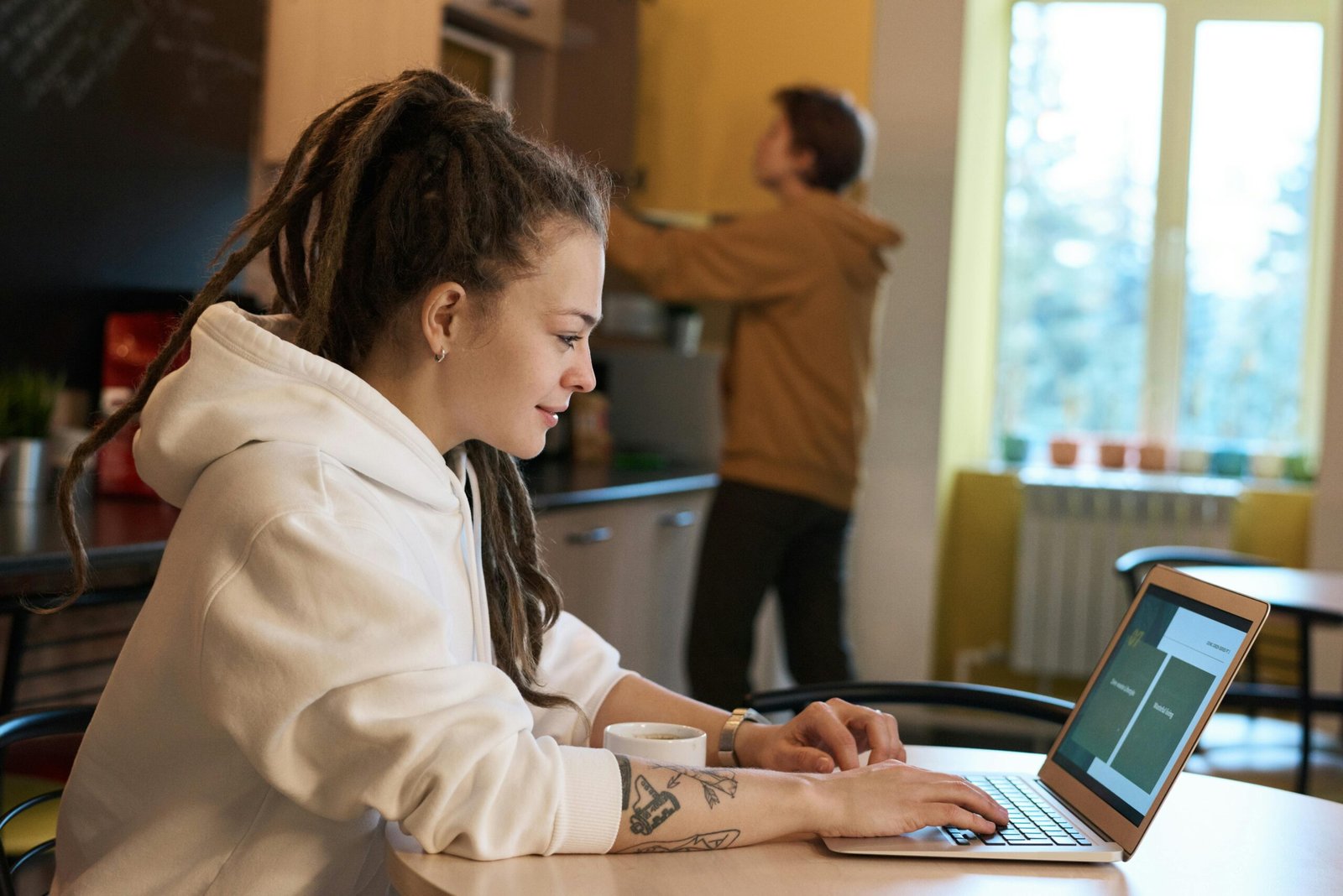 Freelancer with dreadlocks working on a laptop in a cozy kitchen.