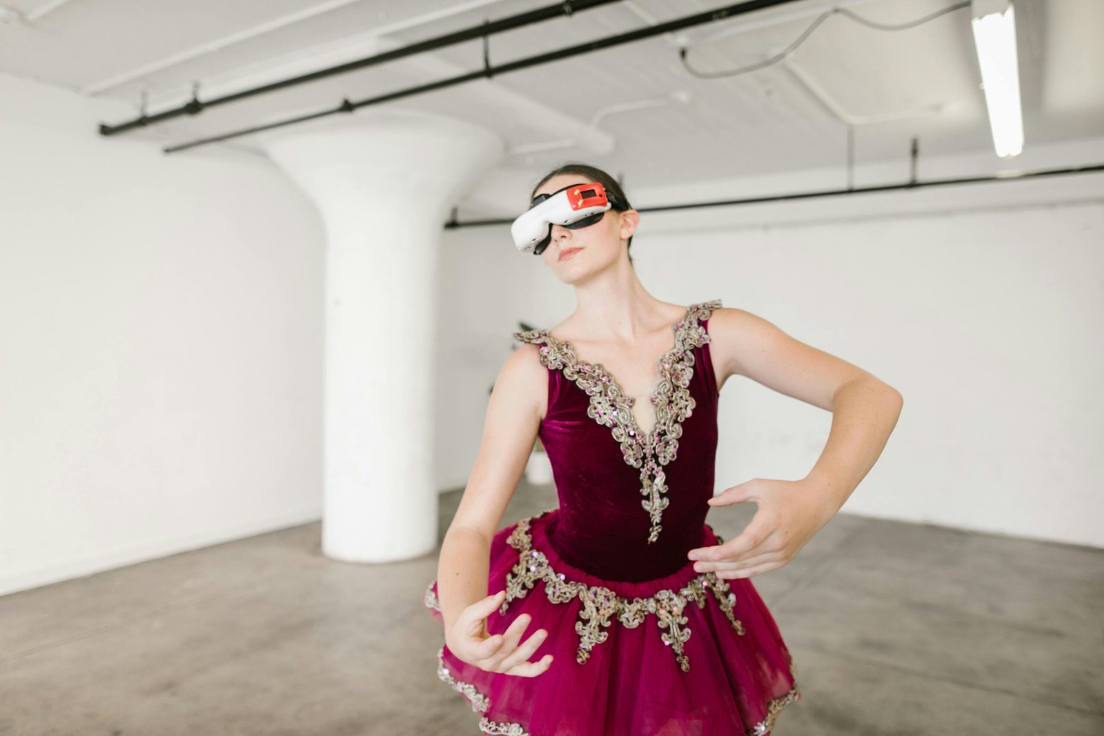 A ballerina wearing a virtual reality headset, dressed in a maroon tutu with intricate gold details, performing in an empty, minimalist studio space