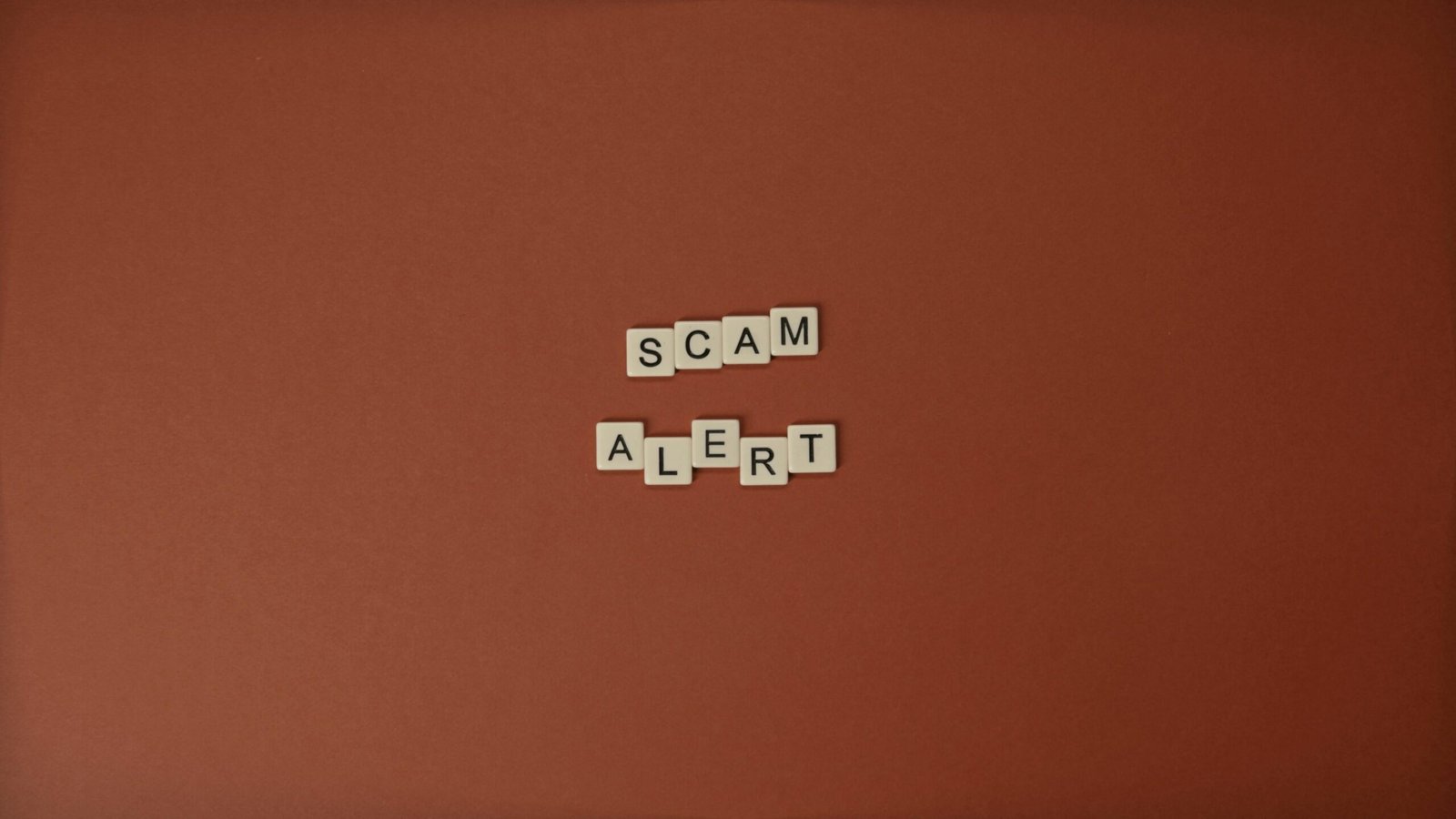 Scrabble tiles spelling 'Scam Alert' on a brown background, symbolizing the importance of awareness in avoiding cryptocurrency scams